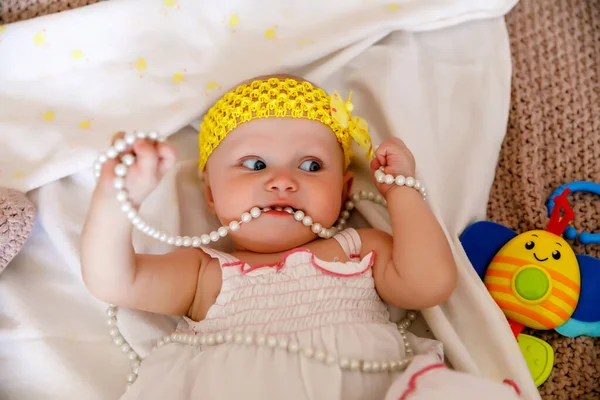 可爱的蓝眼睛6个月大的白衣女孩在床上玩珍珠珠子 漂亮的金发美女迷人的孩子在特写中表现出感情 健康儿童和养育子女的概念 — 图库照片