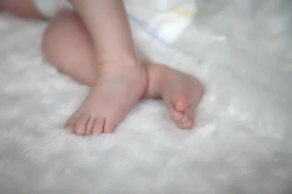 Baby legs and ass in diaper on bed. Leg of newborn. Type of small feet of monthly child. Cute little baby sleeping on white bed at home. Close-up of legs. Concept of new life