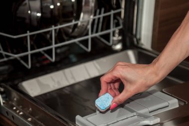 Kız tableti bulaşık deterjanıyla birlikte kutuya koyuyor. Kirli bulaşıkları bulaşık makinesine yükleme işlemi. Evde temizlik ve düzen var. Ev konforu ve düzen kavramı. Metin veya logo için boşluk