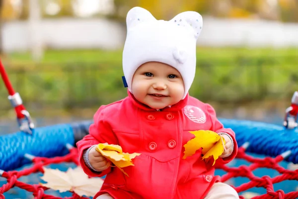 孩子们骑着黄色的秋叶荡秋千 可爱的蓝眼睛的一岁小女孩 身穿红衣 头戴白帽 迷人的婴儿在特写中表现出感情 健康儿童和养育子女的概念 — 图库照片