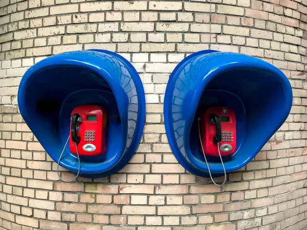 An old Soviet city telephone box on white brick wall. Red metal phone on blue plastic stand. Push-button retro phone. Old phone booth
