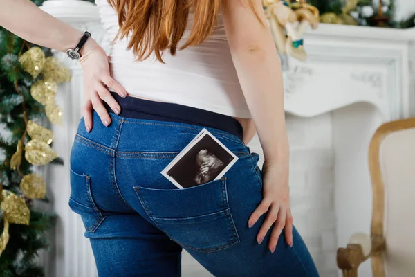 In the back pocket of your jeans, an ultrasound scan of babies. Close-up of woman\'s ass in jeans on light background. Happy family pregnancy, waiting. Black and white photo scanning