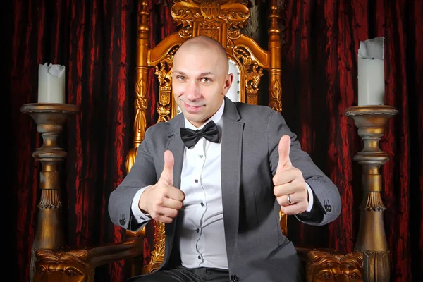 Made businessman gives thumbs up sign that he likes or approves of something on throne in interior background. Concept of good business. Showman and giving thumbs up. Copyright space