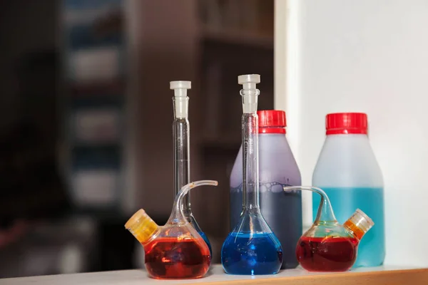 化学実験室でのフラスコと試験管のグループ 実験のための実験台上の試薬とサンプル酸懸濁液 内部に異なる色のサンプルを持つ様々な円錐形のフラスコ — ストック写真