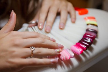 İyi bakımlı kadınlar tırnak rengi örnekleri seçer. Beyaz masadaki, tırnak rengi paletli güzellik salonunda kadın eli. Çivi tedavisi ve bakım. Tarz ve güzellik tatmini kavramı