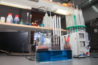 Kimya laboratuvarında elektroliz için ekipman. Laboratuvar masasına deney için akım sağlayan reaksiyonlar ve cihazlar. İç kısımda montaj ve çeşitli konik şişeler ve test tüpleri.