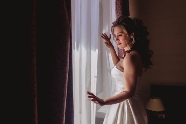 Güzel genç gelin, otel odasının penceresinde bekliyor. Gelinin düğün gününün sabahı. Mutlu gelin, damatla tanışmak için bekle. Telif Hakkı Boşluğu