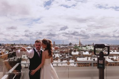Gelin ve damat, panoramik manzarası olan eski kasabayı çatıda kucaklıyor. Güneşli düğün gününde gelinlik giyen yeni evliler. Çatıda muhteşem manzaralı bir çift. Şehrin arka planında aşık yeni evliler