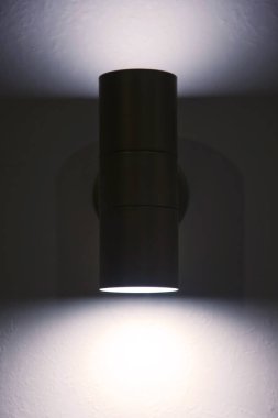 Beyaz desenli duvarda modern bir lamba. Gri duvarda parlayan krom lamba. Yazı için arka planda boş alan ve koyu şerit. Site veya afiş için telif hakkı alanı