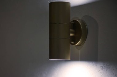 Beyaz desenli duvarda modern bir lamba. Gri duvarda parlayan krom lamba. Yazı için arka planda boş alan ve koyu şerit. Site veya afiş için telif hakkı alanı