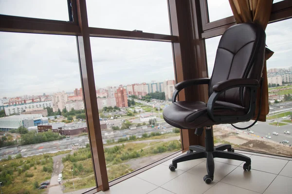 Leather office chair on glass balcony with landscape view of large city or metropolis. Concept of work at home or unemployment. Copyright space for site or banner