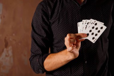 Kumar kartları olan genç bir adamın yakın plan portresi. Yakışıklı adam kartla numara yapıyor. Metal desenli arka planda sihirbazın akıllı elleri. Eğlence ve hobi anlayışı. Telif Hakkı Boşluğu