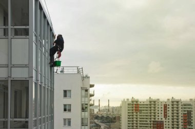 Endüstriyel dağcılık işçisi dış cephe camlarını yıkarken konut binasının üzerinde asılı duruyor. İp erişimi olan işçi ev duvarında asılı. Şehir işleri kavramı. Boşluğu kopyala