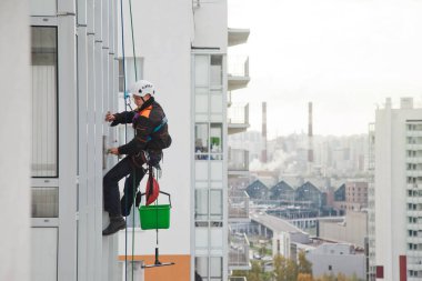 Endüstriyel dağcılık işçisi dış cephe camlarını yıkarken konut binasının üzerinde asılı duruyor. İp erişimi olan işçi ev duvarında asılı. Şehir işleri kavramı. Boşluğu kopyala
