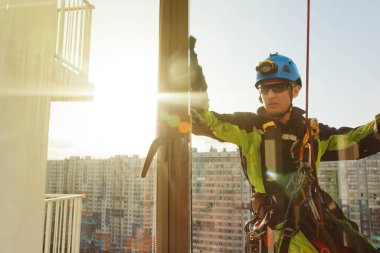 Endüstriyel dağcılık işçisi dış cephe camlarını yıkarken konut binasının üzerinde asılı duruyor. İp erişimi olan işçi ev duvarında asılı. Şehir işleri kavramı. Boşluğu kopyala