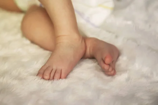 Baby legs and ass in diaper on bed. Leg of newborn. Type of small feet of monthly child. Cute little baby sleeping on white bed at home. Close-up of legs. Concept of new life