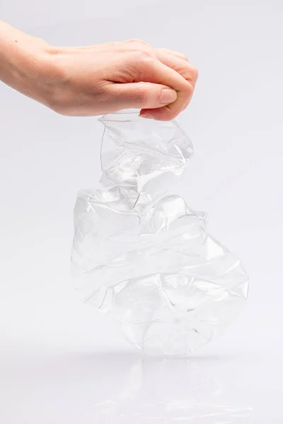 Close-up of a white people\'s hand crushing a crumpled plastic bottle in front of a white background
