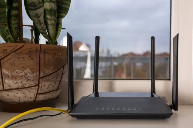 Pencerenin kenarında siyah bir Wi-Fi yönlendirici duruyor.
