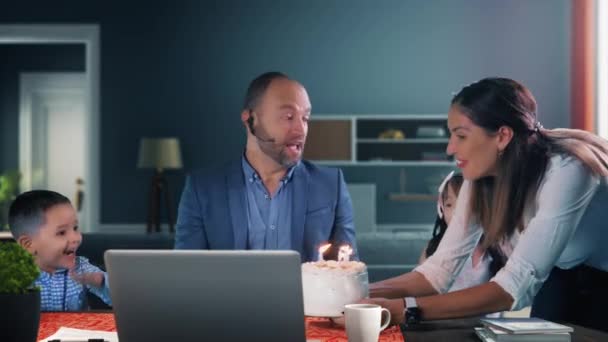 家族は彼が自宅からノートパソコンに取り組んでいる間にケーキを持ってくる父親の誕生日を祝います 妻と息子と娘はビデオ会議中に父親を驚かせ — ストック動画