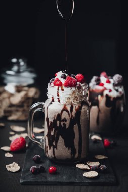 Koyu arkaplanda çikolatalı milkshake ve üstünde kırmızı böğürtlen.