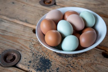 Tahta bir masada beyaz bir kasede doğal renklerde tavuk yumurtası.