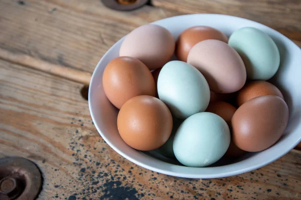 An assortment of Naturally Colorful Chicken Eggs in a white bowl on a wooden table