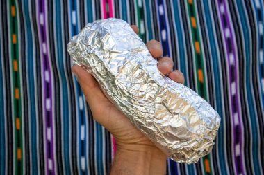 Büyük California usulü Burrito folyoya sarılı ve bir elde tutuluyor.