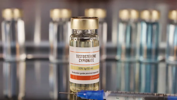 Vial of testosterone cypionate and syringe on a stainless steel background