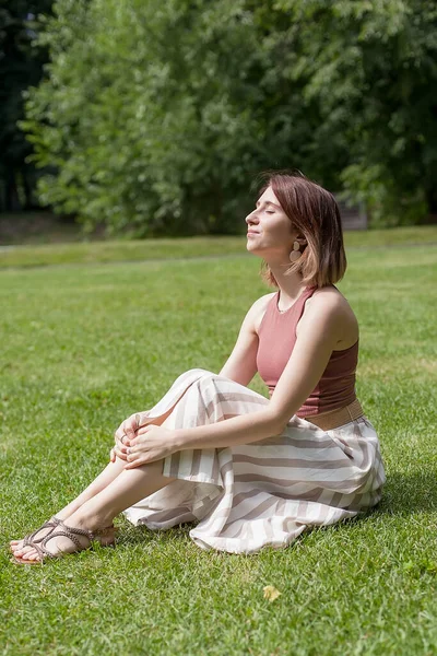 Portret dziewczyny na zielonym polu. Kobieta siedzi na trawie i zamknęła oczy. Letni dzień. Relaks. — Zdjęcie stockowe