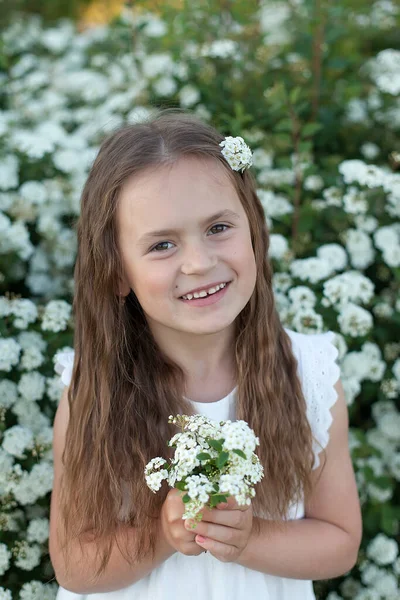 小さな笑顔の女の子は 夕日の庭で白い花の花束 春の開花公園で立っています — ストック写真