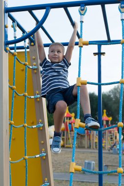 Oyun bahçesinde ip merdivene asılmış küçük bir çocuk. Temiz havada oyunlar.