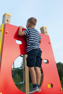 Bir çocuk oyun parkında duvara tırmanıyor. Kaya tırmanışı dersleri. Çocukların açık hava oyunları.