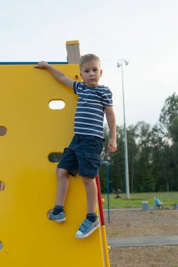 Sevimli bir çocuk oyun alanında eğleniyor. Yaz tatili. Bebek çocuk parkına tırmanıyor