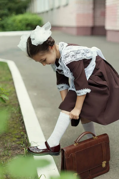 ソ連の制服を着た少女が学校の近くに立って白い膝の靴下を引っ張っている 一年生 — ストック写真