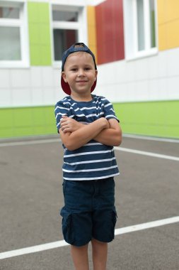 Küçük bir çocuk yalnız yürür, binadan çıkar ve merdivenlerden aşağı iner. Anaokulu.