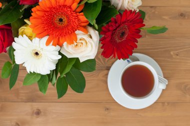 Seramik çaydanlık ve bardaklar ahşap bir masada. Vazoda bir buket parlak çiçek. Kahvaltı.