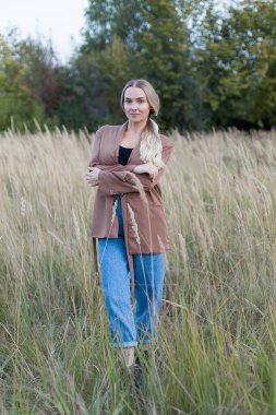 Gün batımında buğday tarlasında duran güzel sarışın kadın kameraya baktı.