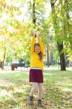 Küçük bir kız, bir sonbahar günü şehir parkında meşe palamudu düşmesin diye ellerini kapatıyor..