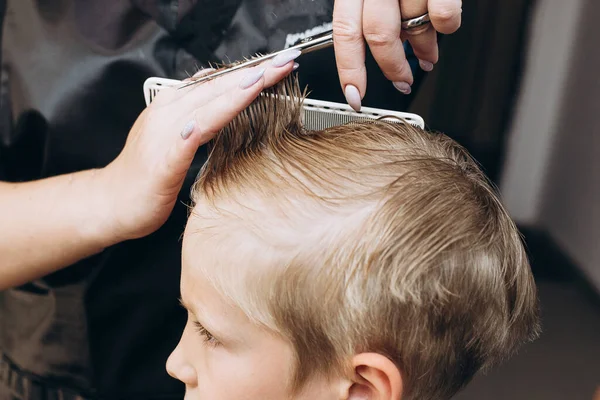 A blond hair boy is hair cutting with barber in the barbershop. Haircut with scissors. Self-care. Close-up haircut. . High quality photo