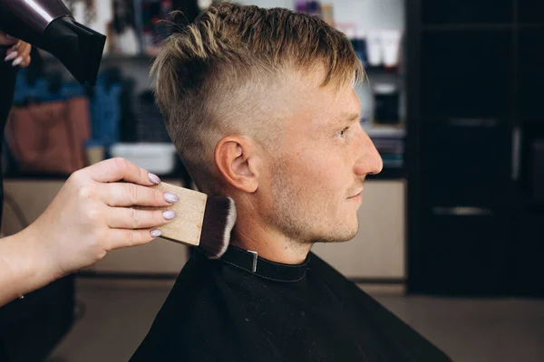 A blond hair man is hair cutting with barber in the barbershop. Haircut with a brush. Self-care. Close-up haircut