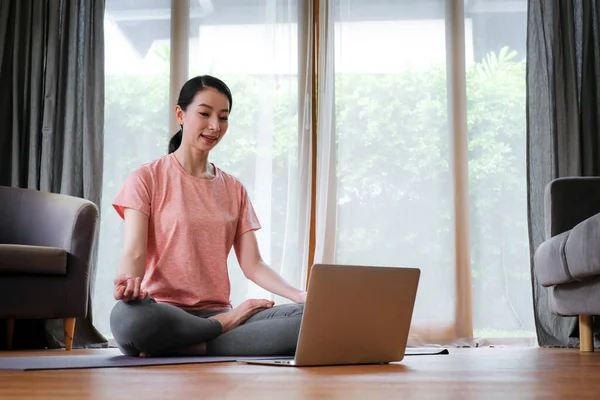 Evde otururken bilgisayarla yoga kursu alan Asyalı bir kadın..