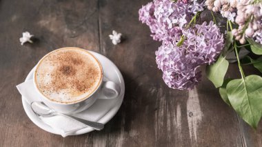 Kapuçino ve tarçın, sehpanın üzerindeki kahve dükkanında leylağın yanında. Seçici odak