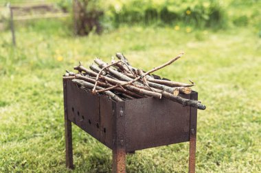 Yeşil otların arka planında ateş yakmak için kuru dallarla dolu paslı bir barbekü.