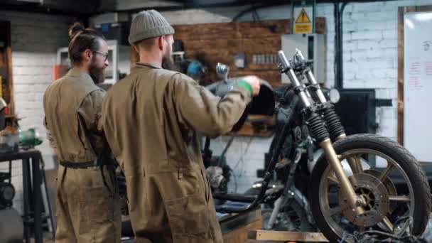 A reparar a bicicleta. Dois homens com barba estão criando motocicleta personalizada — Vídeo de Stock