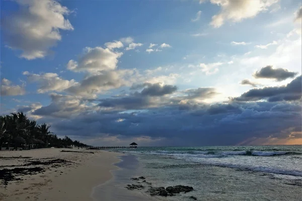 カリブ海で夜明け 昇る太陽は雲のオレンジを描いた 波は砂浜に泡を残します 遠くにはヤシの木のシルエットと水の上に木製の天蓋があります メキシコ — ストック写真