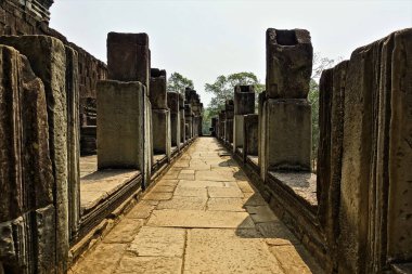 Angkor tapınağının kalıntıları. Kale terasındaki taş galeri dümdüz devam ediyor. Her iki tarafta da harap kolonlar var. Uzakta, orman ve mavi gökyüzü görülebilir. UNESCO Mirası. Kamboçya.