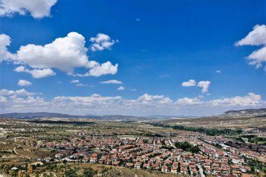 Yukarıdan gelen kapadokya. Yaz, güneşli bir gün. Vadide bir köy var, birçok kırmızı çatısı olan evler. Etrafta alışılmadık kayalar ve güzel dağlar var. Manzaralı bulutlu mavi gökyüzü. Türkiye.