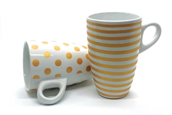白い背景に2つのセラミックカップ マグカップが一つ横になっていて もう一つは立っている 黄色の円とストライプ — ストック写真