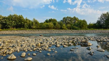 Yaz mevsiminde dağ nehri. Nehir yatağı kısmen kuru. Çakıl taşlarının arasında gökyüzünün yansıdığı bir su gölü var. Ana akımda hızlı bir akım var. Gökyüzüne karşı yeşil ağaçlar. - Rusya. Soçi..