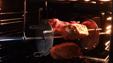 Et elektrikli fırında kızartılıyor. Üç parça domuz eti baharatla işleniyor. Şiş dönüyor. Arka ışık açık..